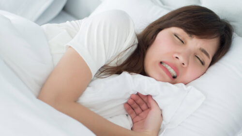 stressed woman with grinding teeth, bruxism symptoms; portrait of stressful, exhausted, tired sleeping woman grinding her teeth with stress; oral, dental care medical concept; asian adult woman model